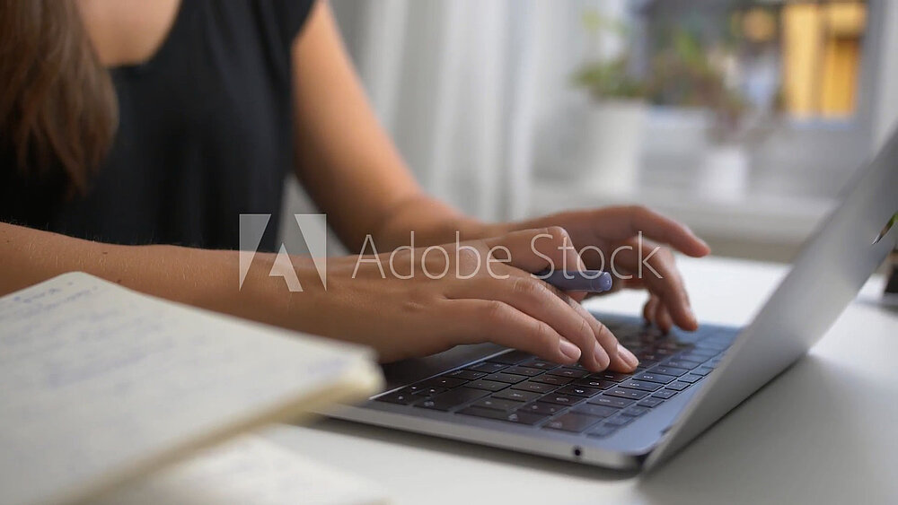Wir sehen auf dem Bild eine Frau, die ein schwarzes T-Shirt trägt. Sie tippt einen Text auf ihrem Laptop ein.